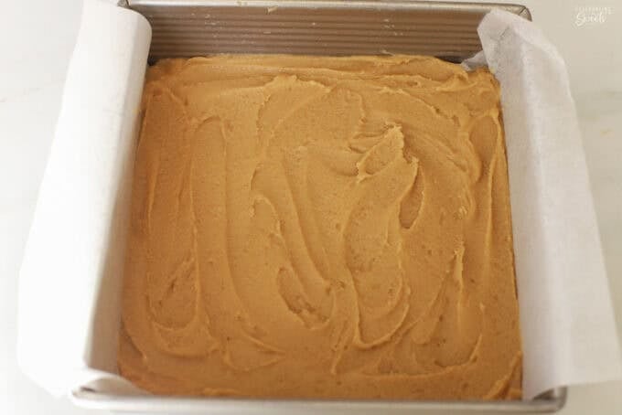 Almond blondie batter in a parchment paper lined baking dish.