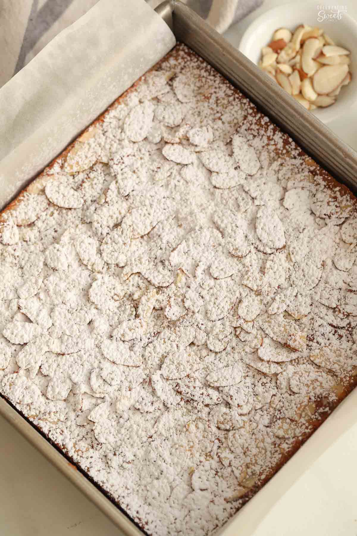 Square pan of almond blondies topped with powdered sugar.