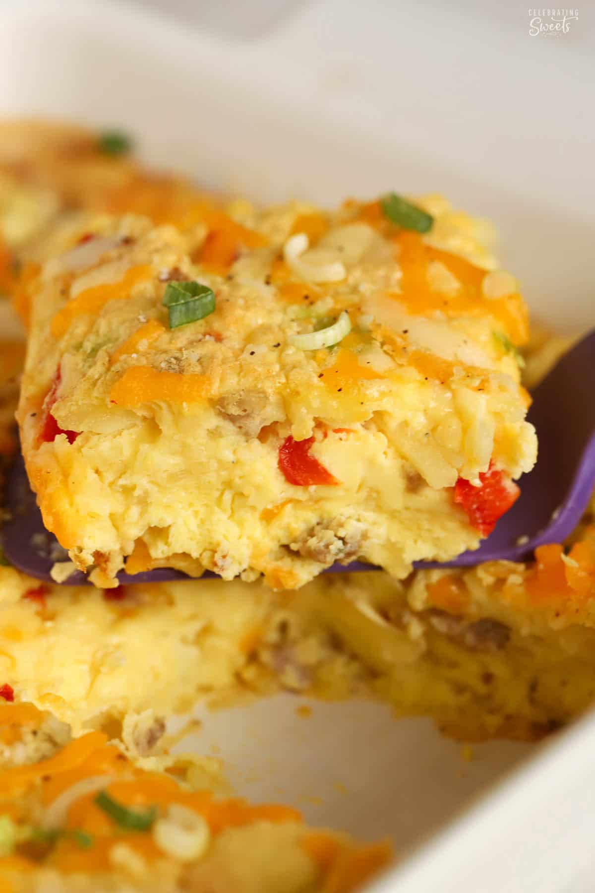 A serving of egg casserole topped with cheese and green onions on a purple spatula.
