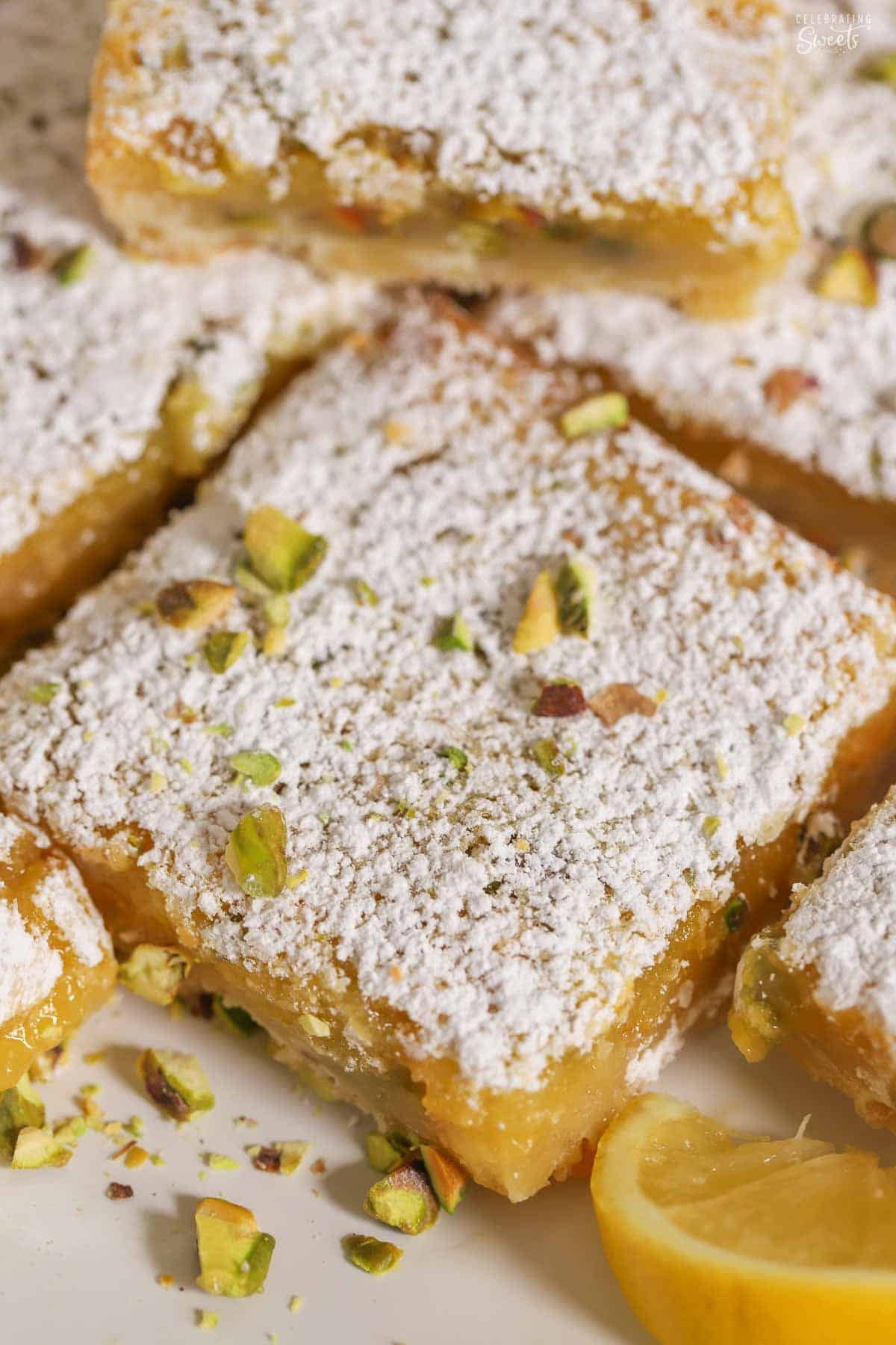 Lemon pistachio bar topped with powdered sugar on a white plate next to a lemon slice.