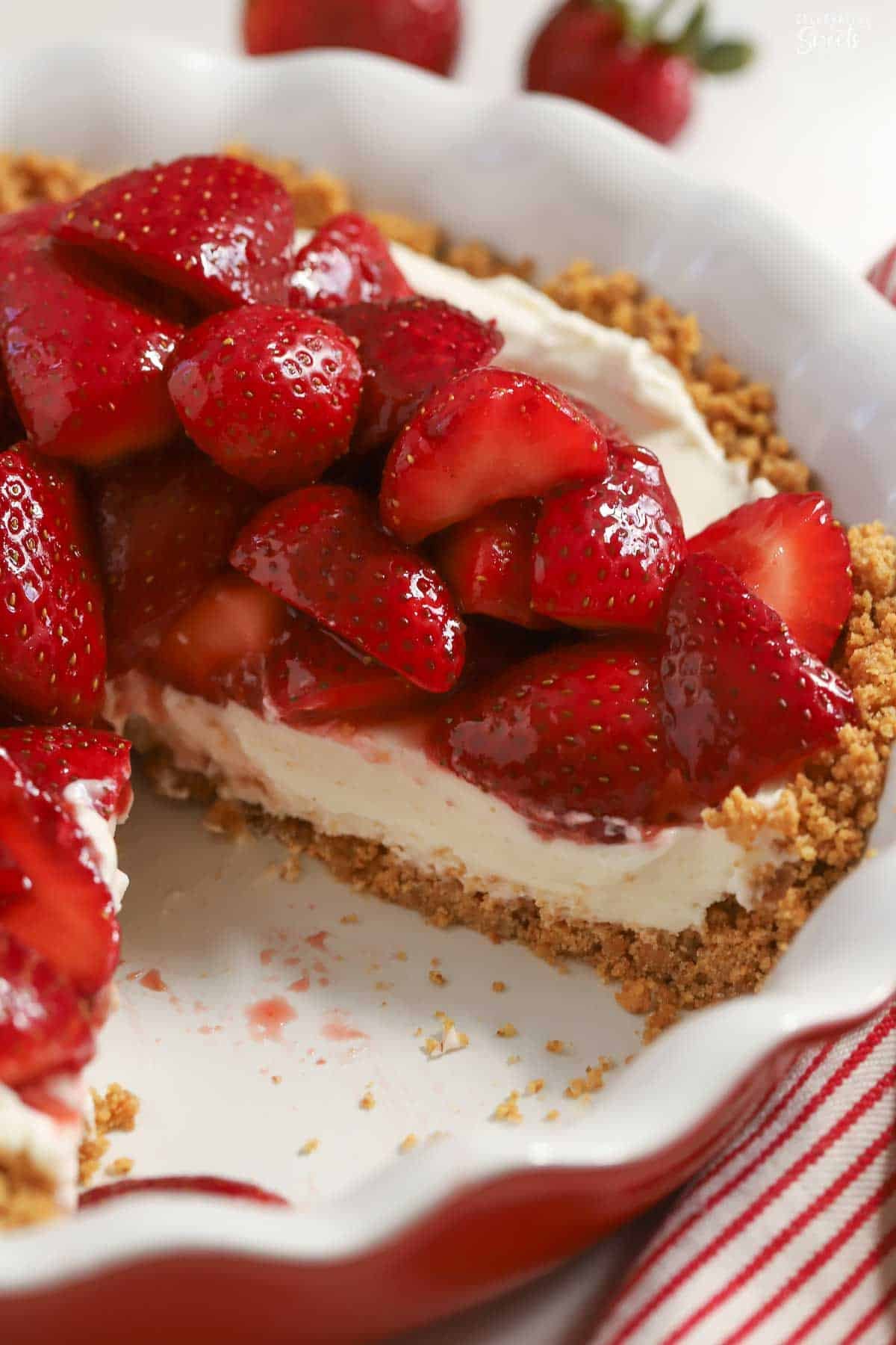 Strawberry cream cheese pie in a red pie plate with a slice removed.