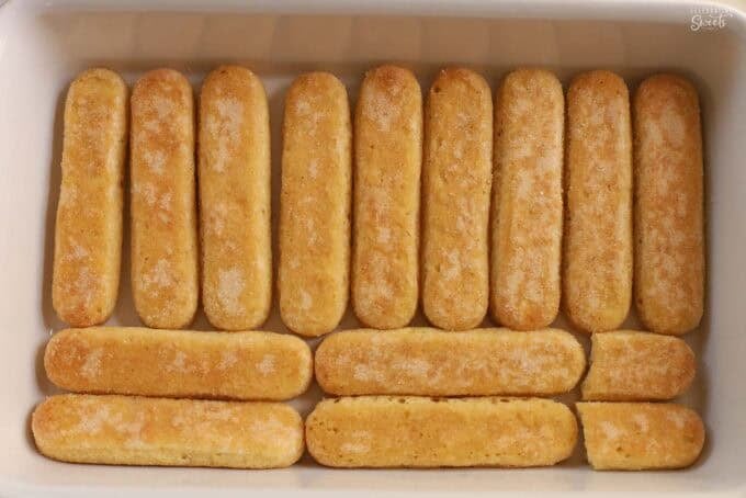 Ladyfingers in a single layer in the bottom of a white baking dish.