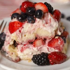Berry tiramisu on a white plate garnished with mixed berries.