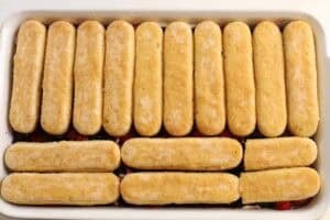 Ladyfingers layered on top of berries in a rectangular baking dish.