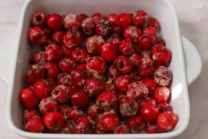 Cherries tossed with sugar and flour in a white square baking dish.