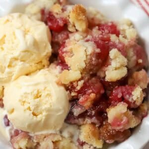Cherry cobbler and two scoops of vanilla ice cream in a white bowl.