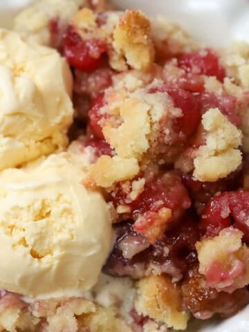 Cherry cobbler and two scoops of vanilla ice cream in a white bowl.