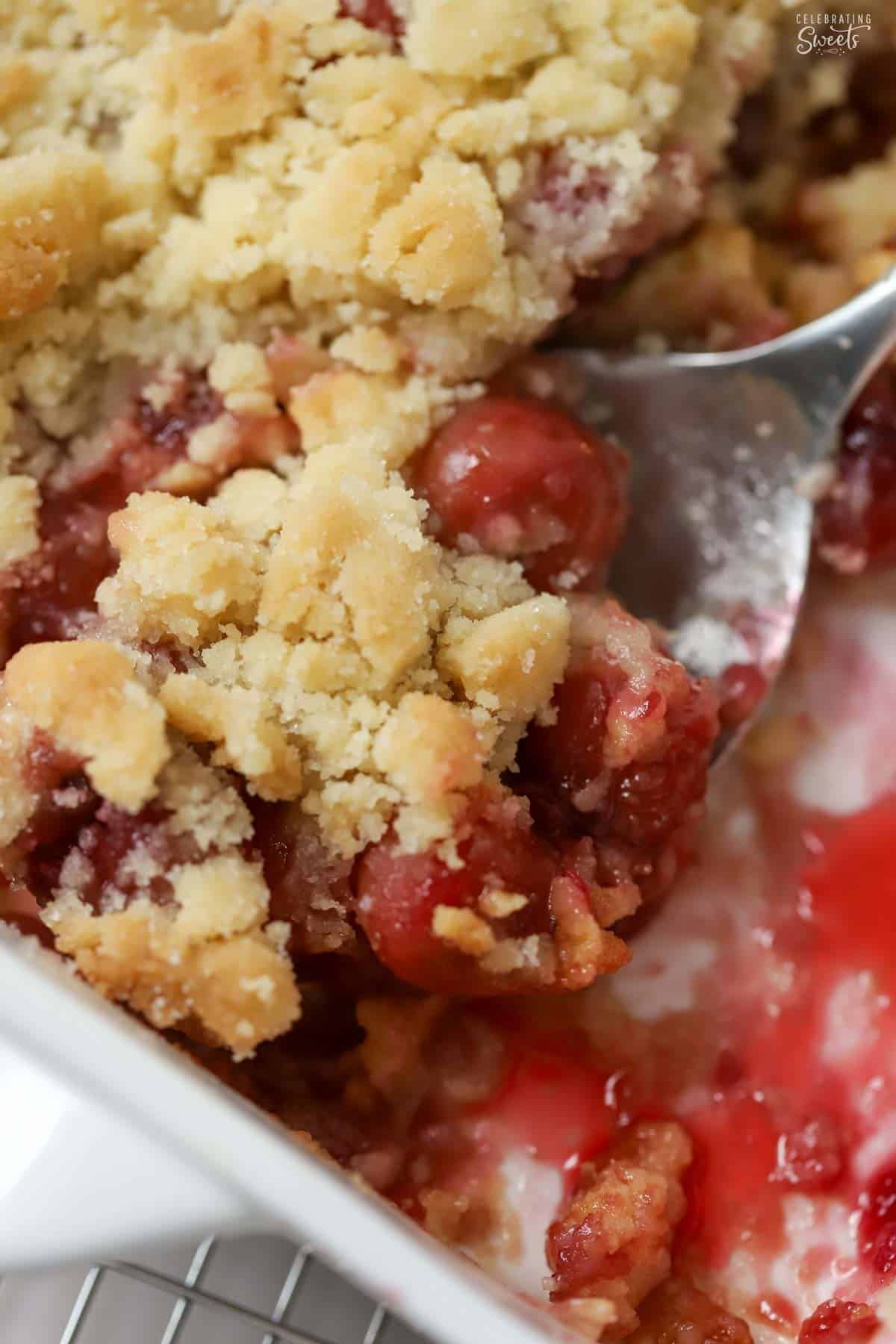 Cherry cobbler on a silver spoon in a white baking dish.
