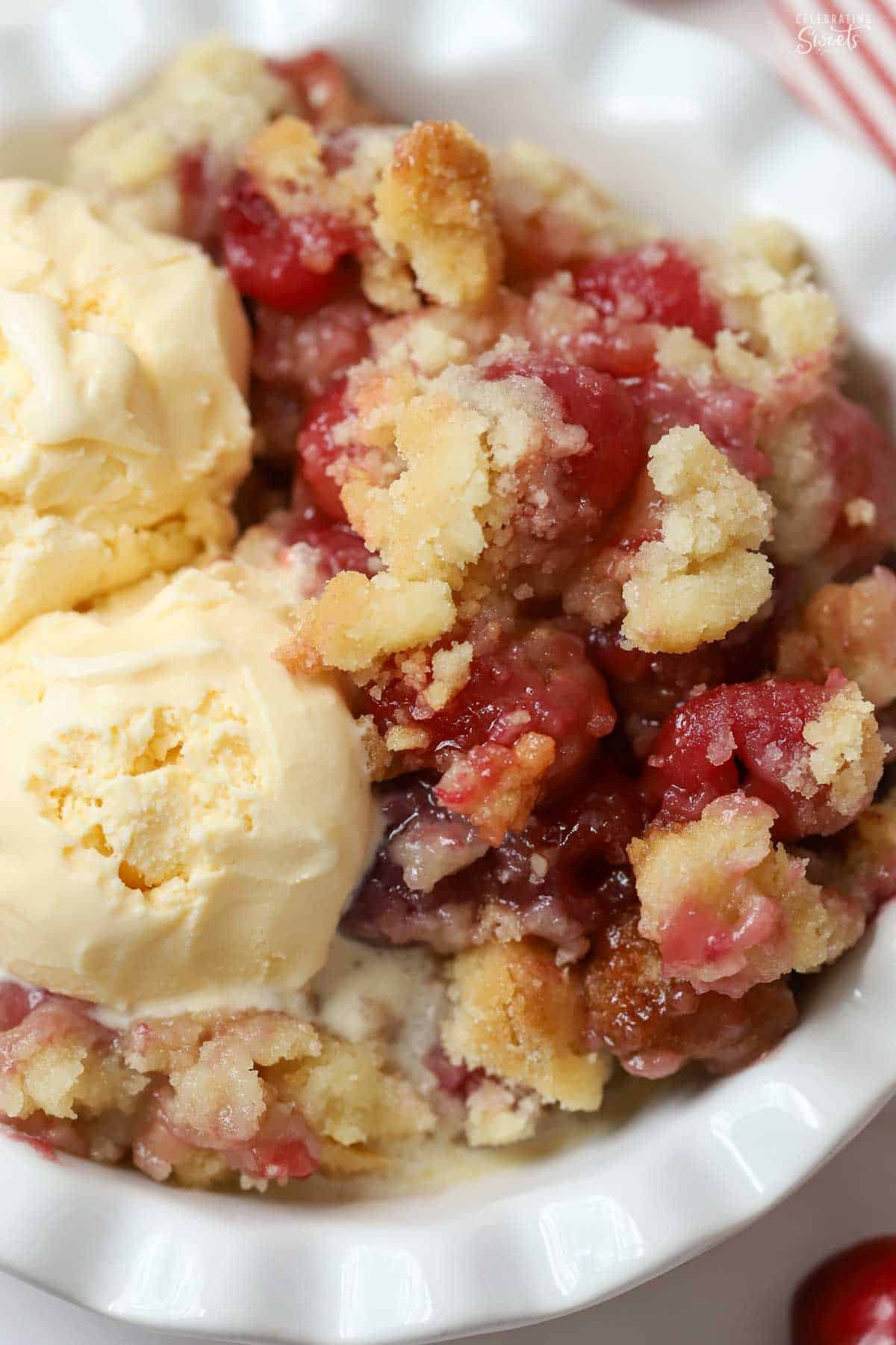 Cherry cobbler and two scoops of vanilla ice cream in a white bowl.