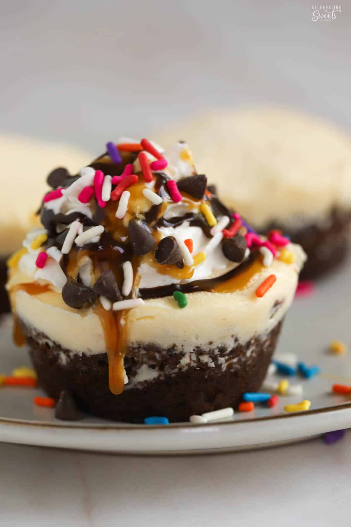 Ice cream cupcake topped with whipped cream and rainbow sprinkles on a grey plate.
