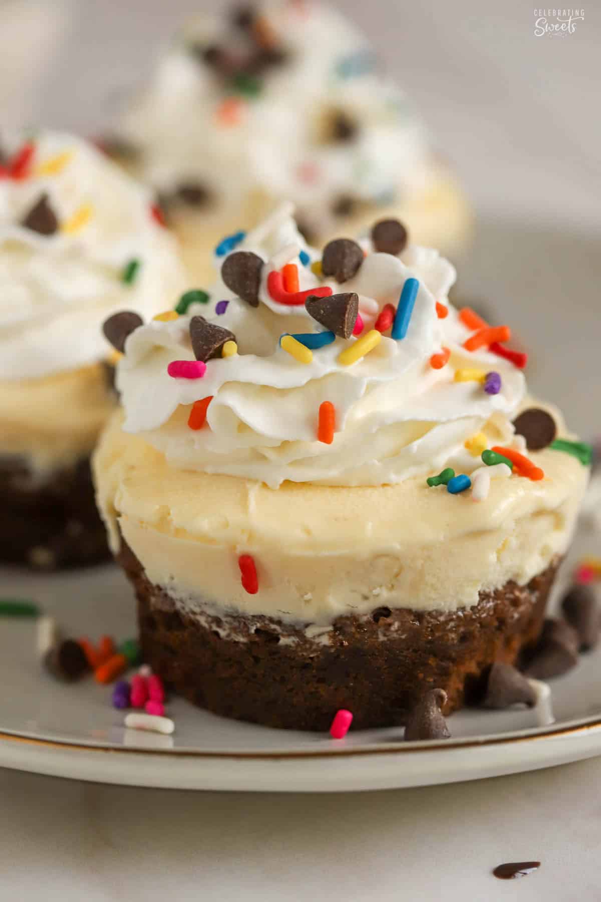 Brownie bottom ice cream cupcake topped with whipped cream and rainbow sprinkles on a grey plate.