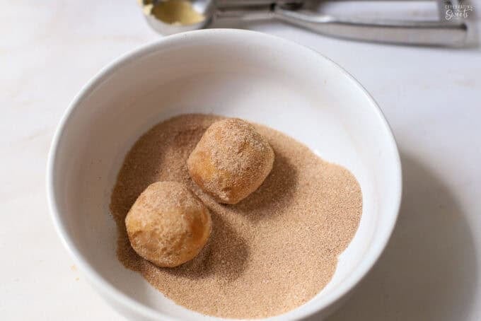 Snickerdoodle cookie dough balls in a white bowl of cinnamon sugar.