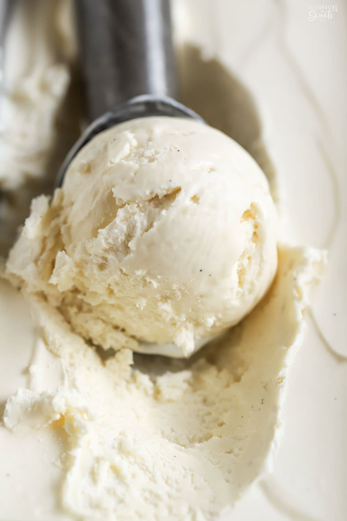 A scoop of vanilla ice cream on a metal scoop inside of a loaf pan.