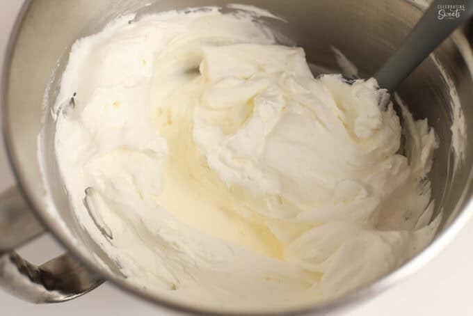 Whipped cream in a metal bowl with a grey spatula.