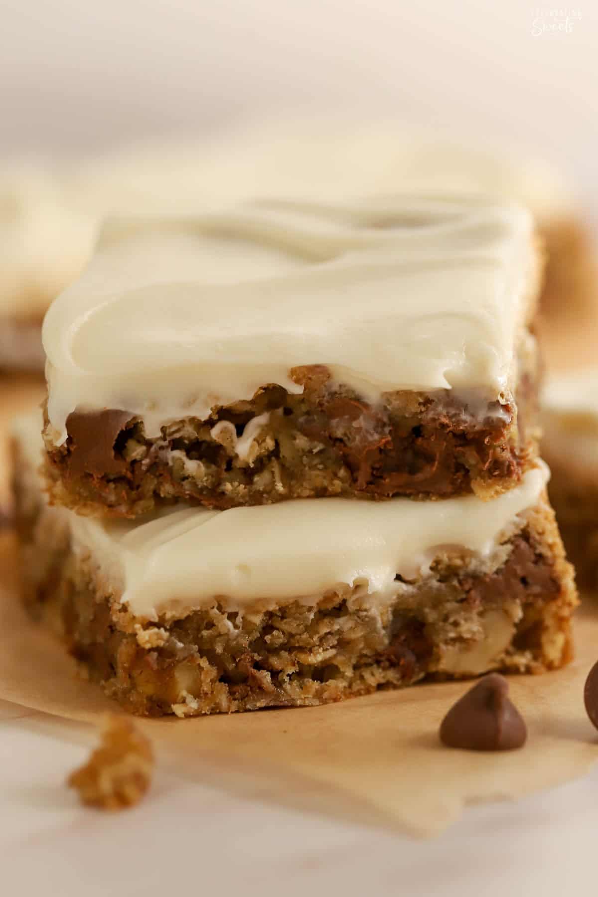 Two oatmeal chocolate chip cookie bars topped with white frosting stacked on top of each other.