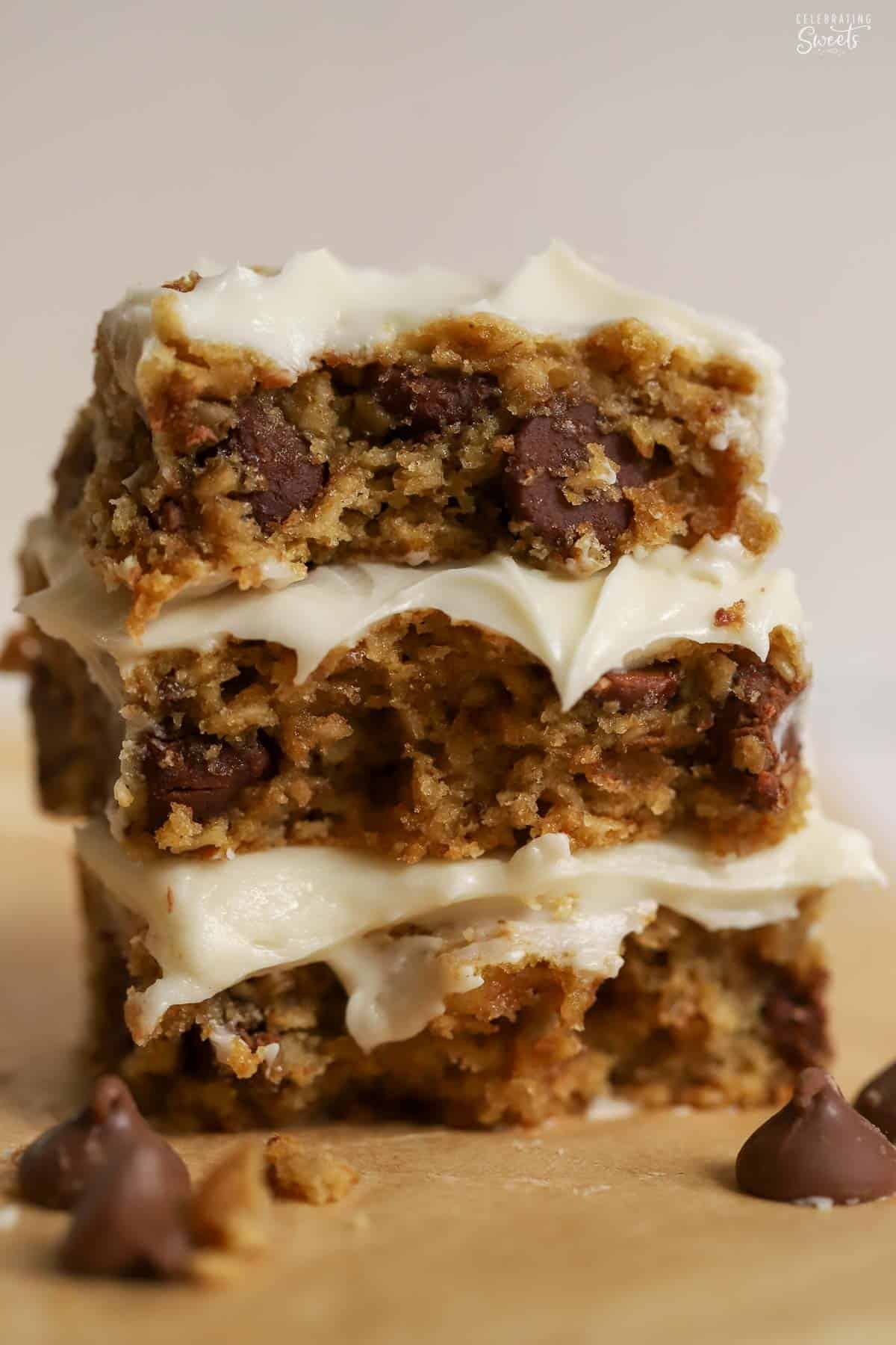 Stack of three oatmeal chocolate chip bars topped with white frosting surrounded by four large chocolate chips.