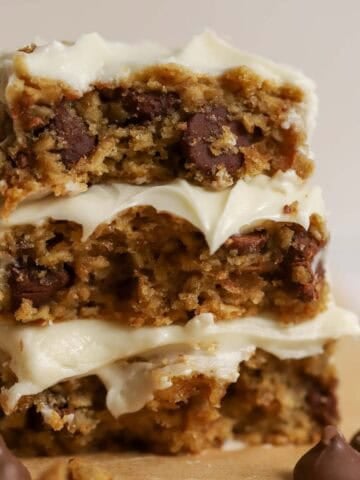 Stack of three oatmeal chocolate chip bars topped with white frosting surrounded by four large chocolate chips.