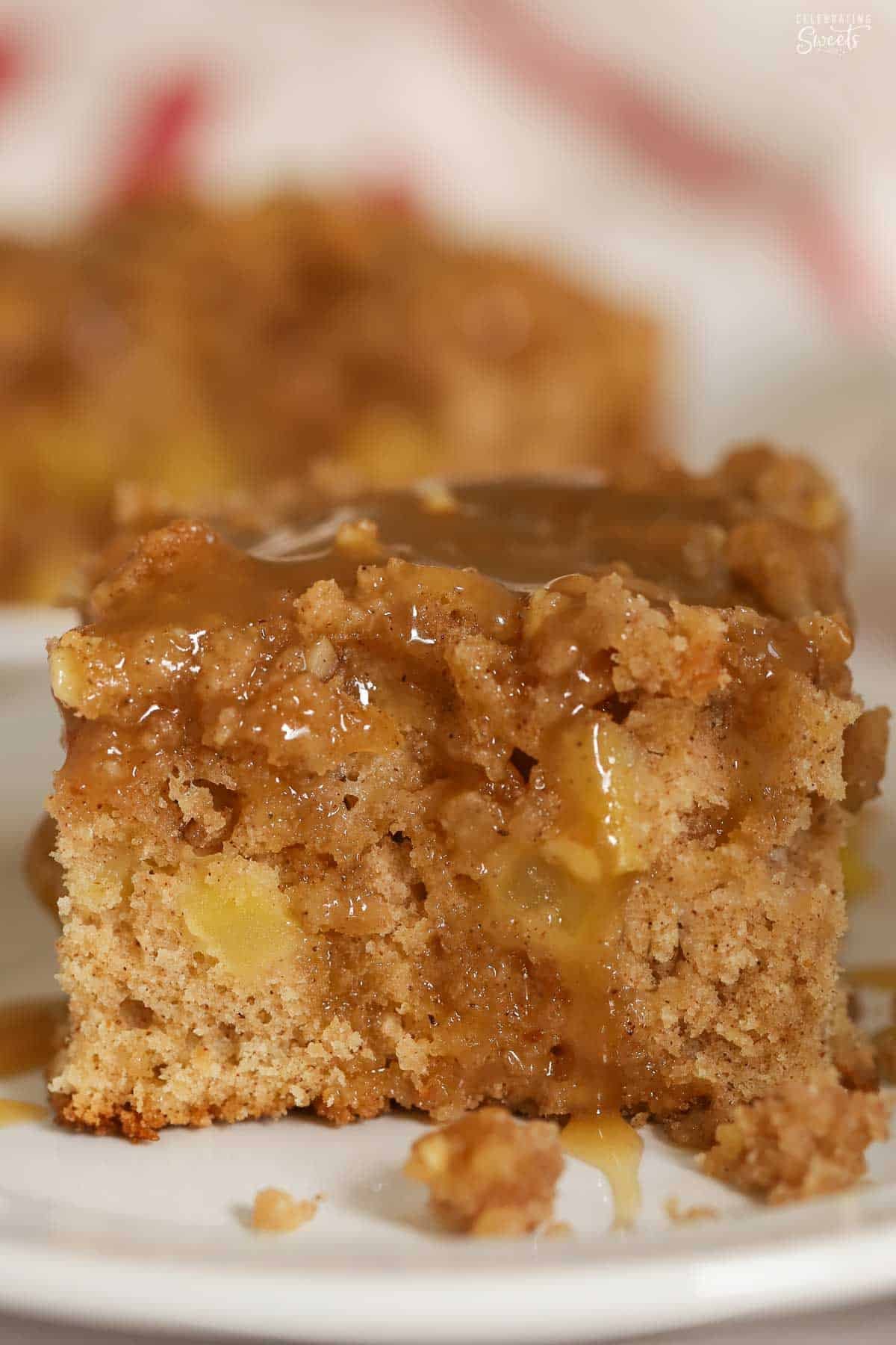 A slice of apple crumb cake topped with brown sugar sauce on a white plate.