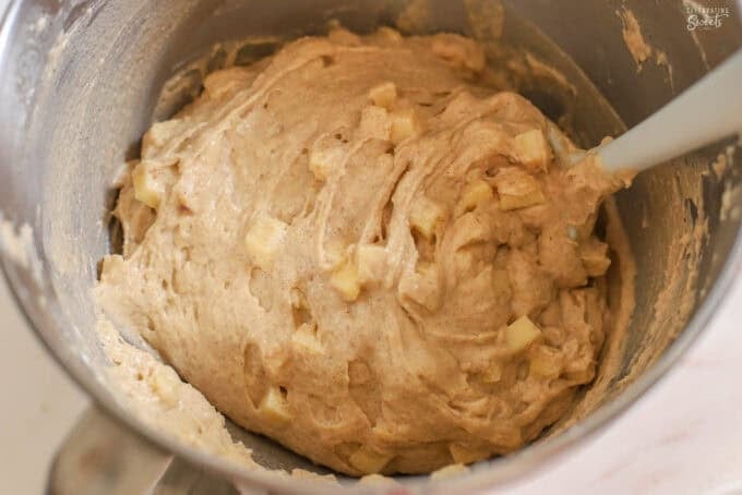 Apple cake batter in a silver bowl with a grey spatula.