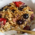 A serving of oatmeal and berries in a white bowl with a gold spoon.