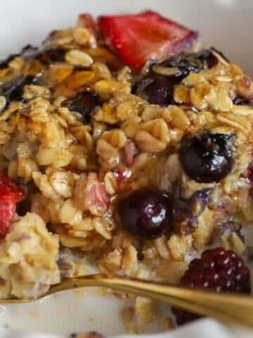 A serving of oatmeal and berries in a white bowl with a gold spoon.