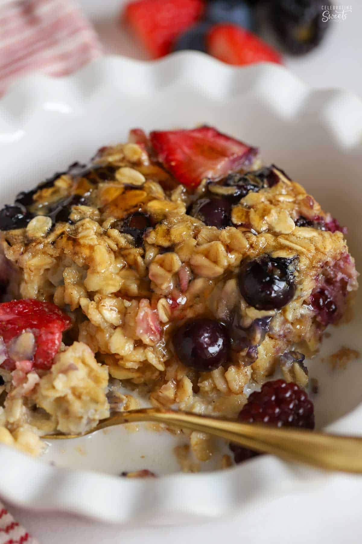 A serving of oatmeal and berries in a white bowl with a gold spoon.