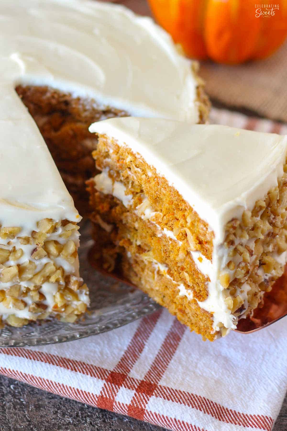 Slice of three layer pumpkin carrot cake topped with white frosting and walnuts on a glass plate.