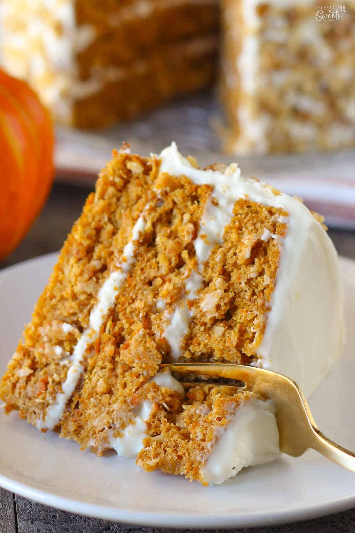 Three layer slice of pumpkin carrot cake on a white plate with a gold fork.