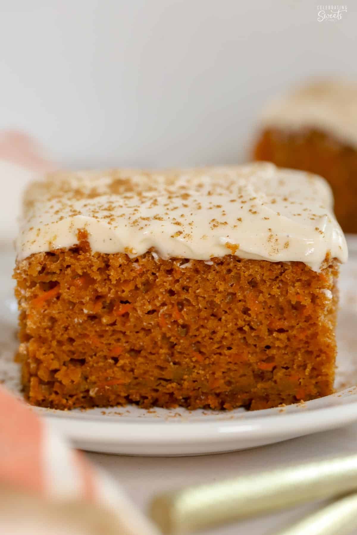 Slice of pumpkin carrot cake on a white plate topped with cream cheese frosting.