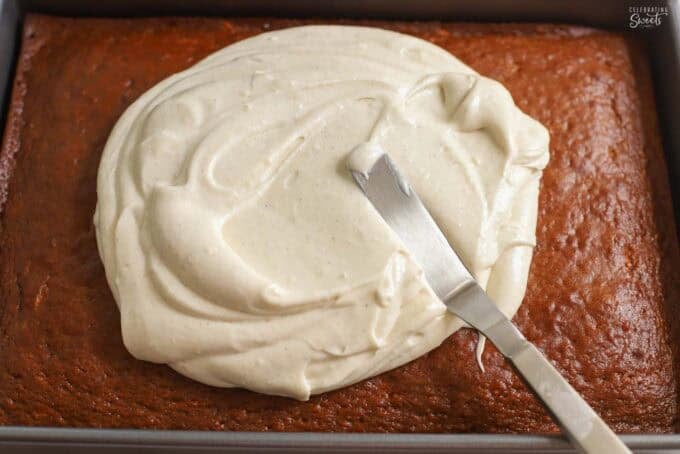 Cream cheese frosting being spread on a rectangular pumpkin carrot cake.