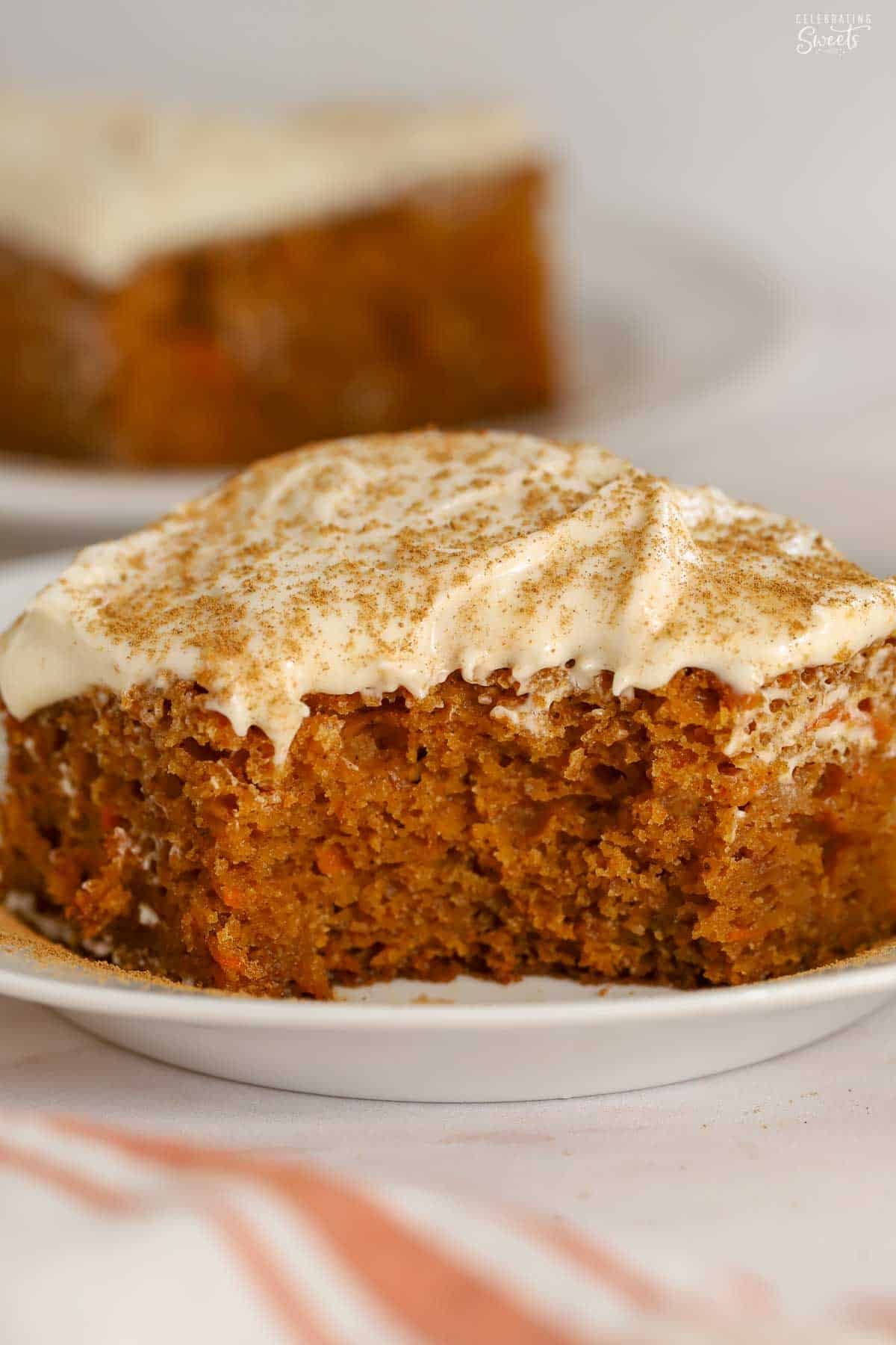 A slice of pumpkin carrot cake on a white plate topped with white frosting and cinnamon.
