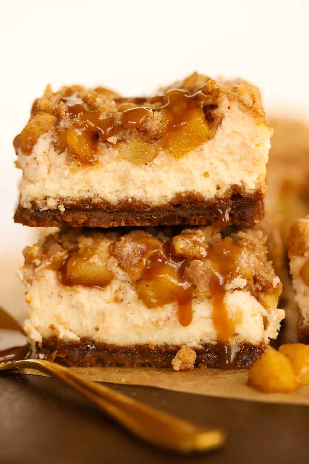 Two apple cheesecake bars stacked on top of each other on a wooden board.