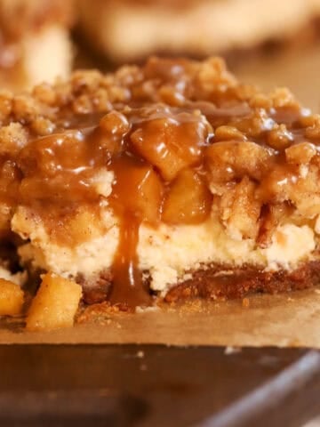An apple cheesecake bar topped with caramel sauce on a wooden board.