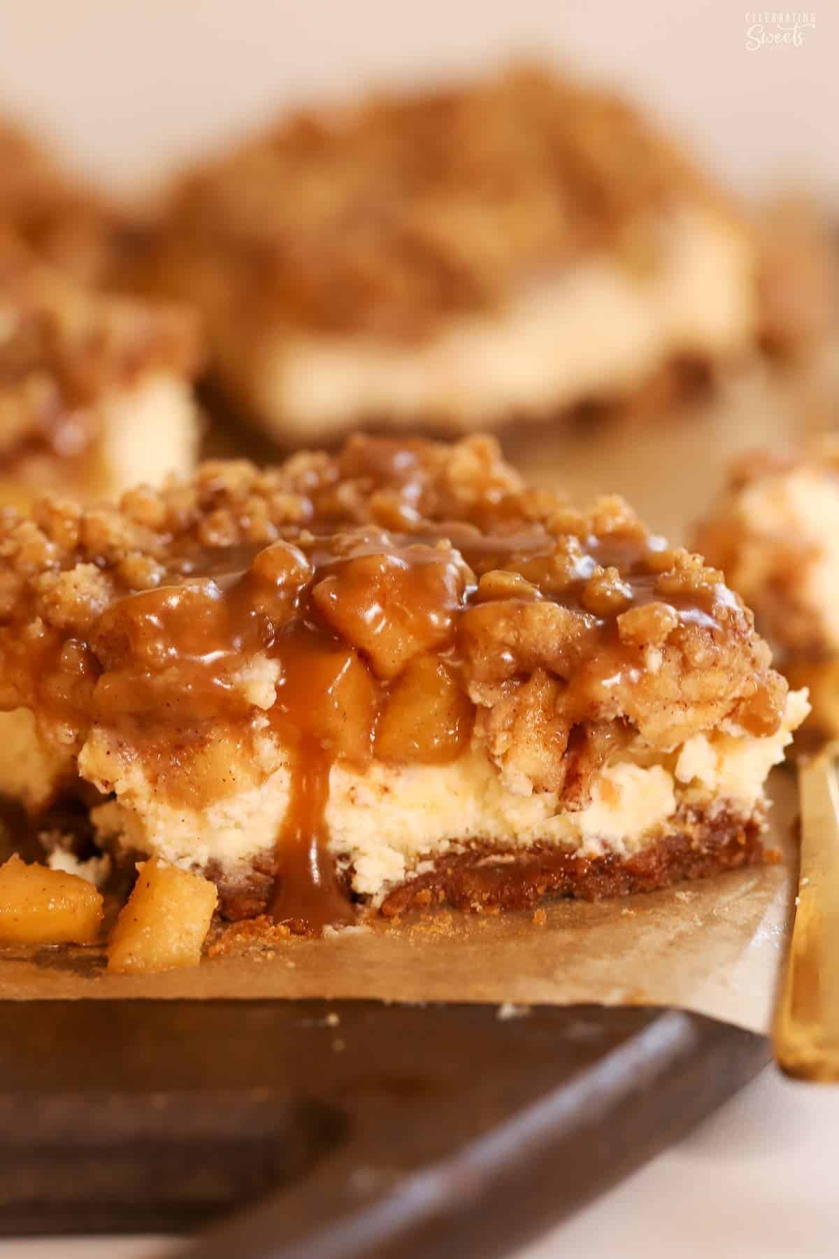 An apple cheesecake bar topped with caramel sauce on a wooden board.