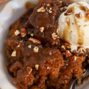 Pumpkin pudding cake in a white bowl topped with a scoop of vanilla ice cream.