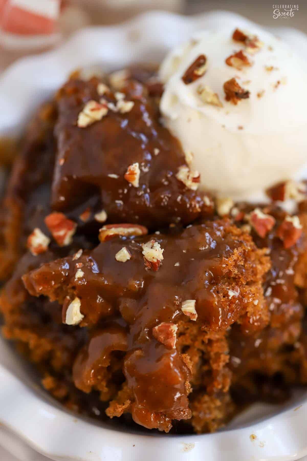 Pumpkin pudding cake topped with a scoop of vanilla ice cream and chopped pecans.