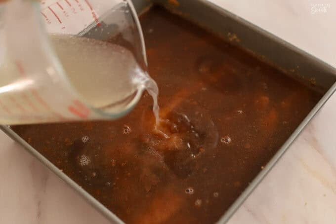 Water being poured over cake batter in a square pan.