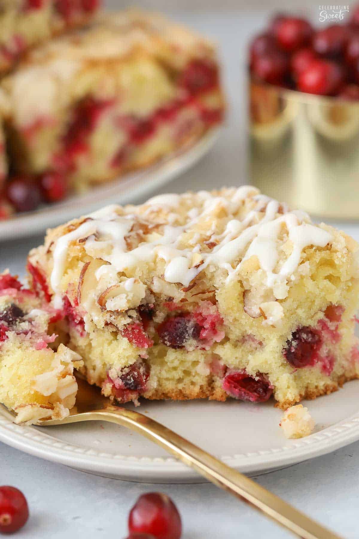 A slice of cranberry cake on a grey plate with a gold fork.