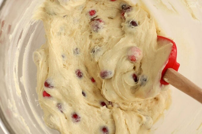 Cranberry cake batter in a glass bowl with a red spatula.