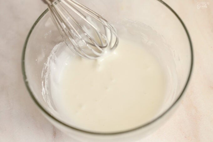 White icing in a glass bowl with a small whisk.