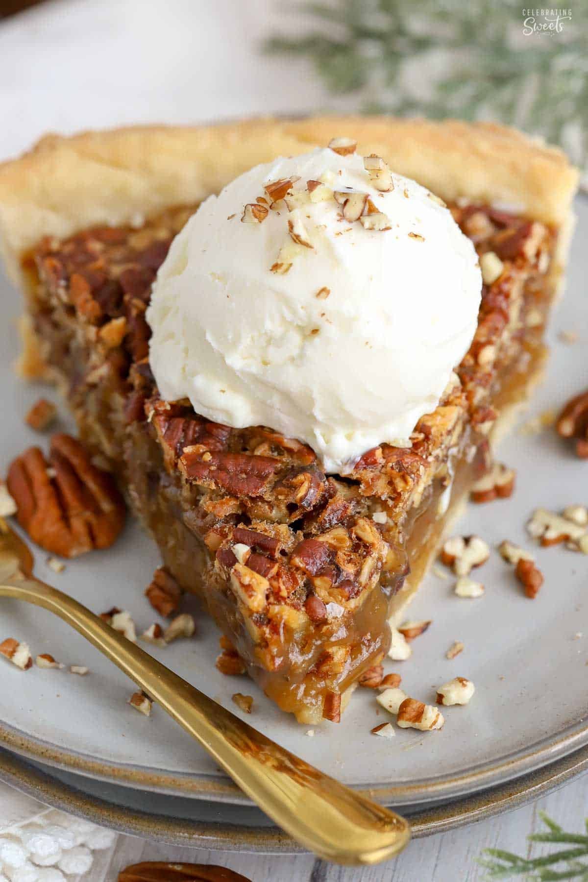 Closeup of a slice of maple pecan pie on a grey plate topped with a scoop of vanilla ice cream.