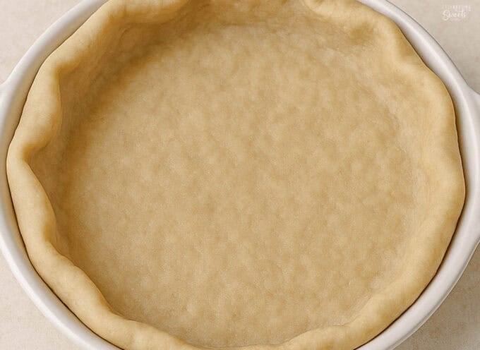 Unbaked pie crust in a white pie plate.