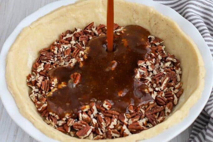 Caramel sauce being poured over pecans in a pie crust.