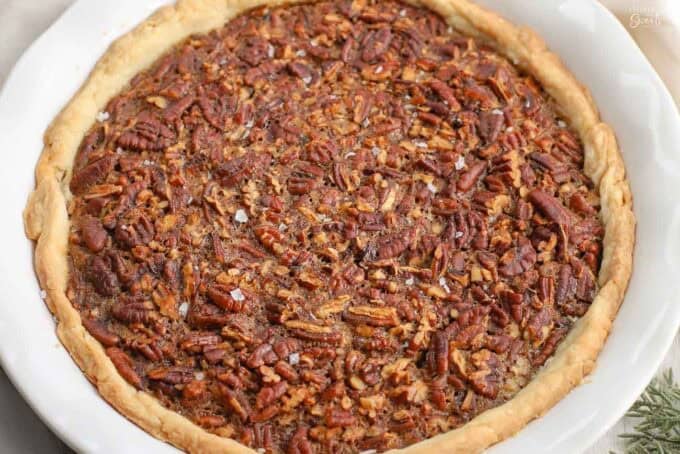 Pecan pie in a white pie plate topped with flakes of salt.