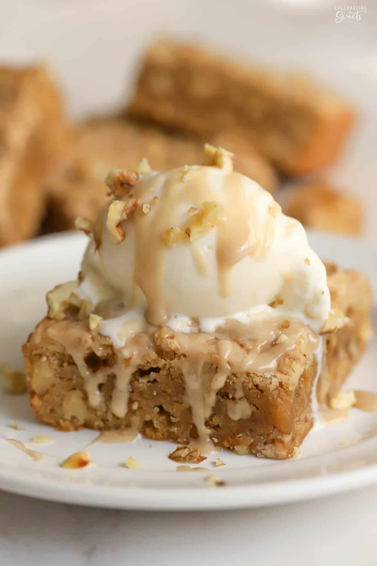 A maple walnut bar on a white plate topped with a scoop of vanilla ice cream and chopped walnuts.
