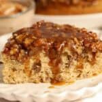 Slice of pecan pie cake topped with caramel on a white scalloped plate.