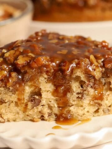 Slice of pecan pie cake topped with caramel on a white scalloped plate.