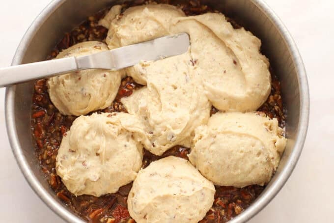 Pecan cake batter being spread over pecans in a round cake pan.