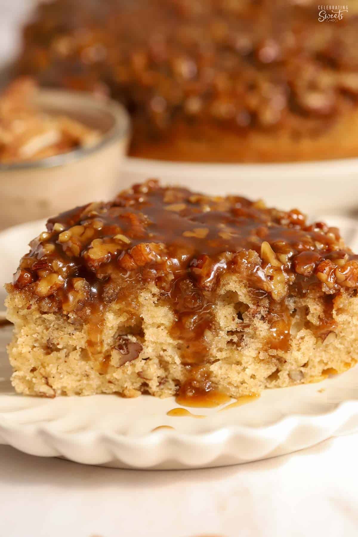 Slice of pecan pie cake topped with caramel on a white scalloped plate.