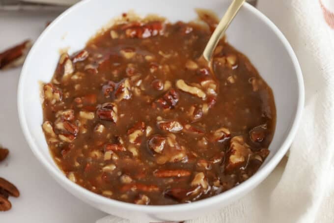 Pecan caramel sauce in a white bowl with a gold spoon.